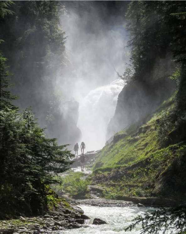 Faraway hikers walk along a creek to a misty waterfall ahead.