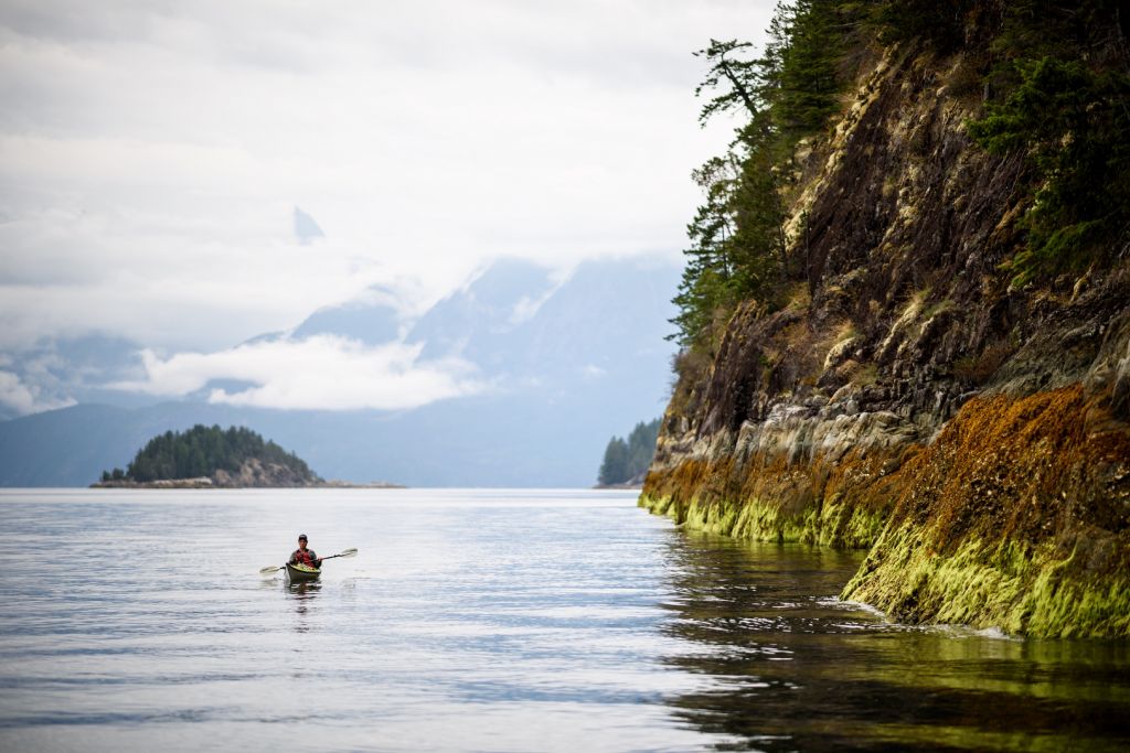 A kayaker paddles along the rugged coastline of Desolation Sound at low tide.