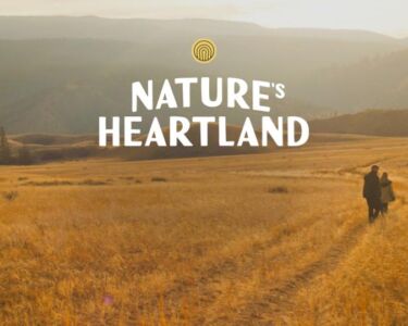 Grassy landscape with two people walking down on a path towards mountains rising in the distance, with a logo overlaid.